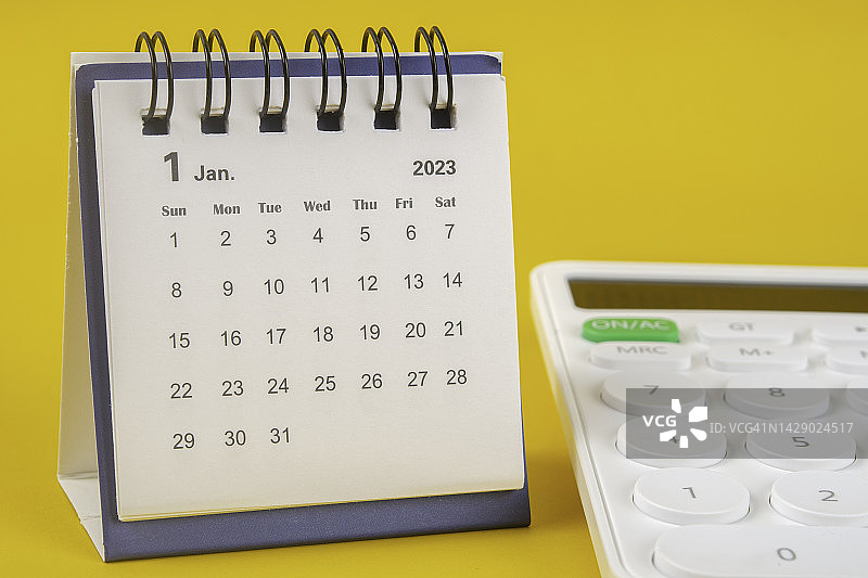 2023日历台:1月是组织者用黄色纸背景下的白色计算器计划和截止日期的月份。图片素材