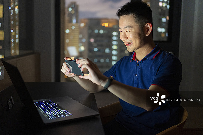 亚洲男子晚上在家里用笔记本电脑和手机工作图片素材