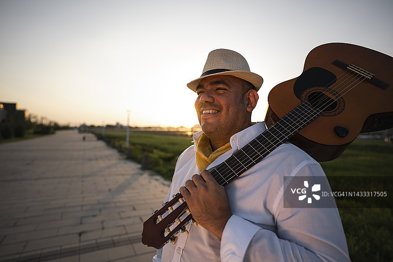 微笑的街头音乐家戴着帽子，肩上扛着吉他图片素材