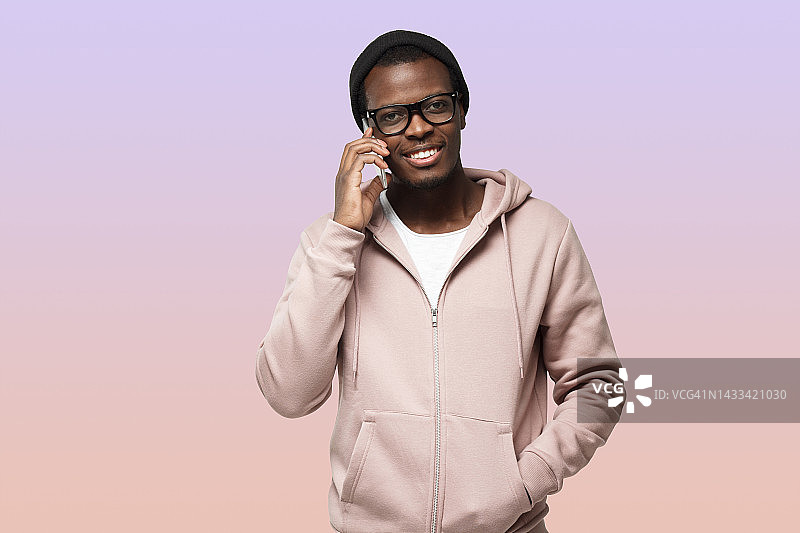 迷人的黑人男性孤立在紫色，把智能手机放在耳边，和朋友说话图片素材