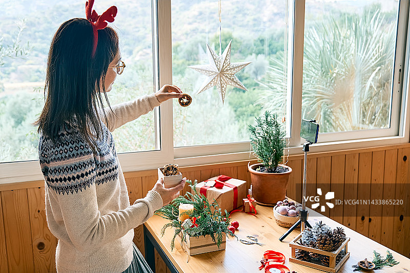 女花匠博主在她的智能手机前用新鲜的松枝、蜡烛和圣诞装饰制作冬季花道。小生意。季节性冬季车间。图片素材