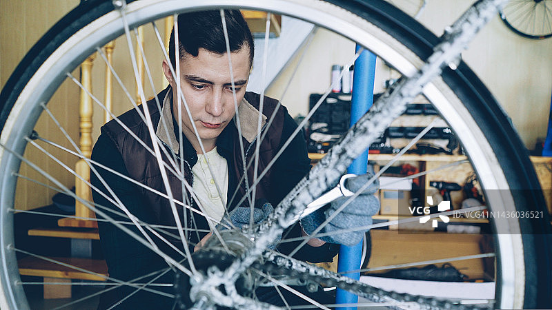 专注的技工正在用扳手修理自行车车轮，同时工作在他的工作场所。自行车维修，人与职业观念。图片素材