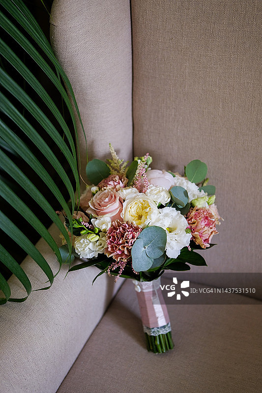 漂亮的婚礼花束放在豪华的天鹅绒椅子上，特写。花束不同的花朵和绿叶，用缎带系，模糊的背景。婚礼的主题。图片素材