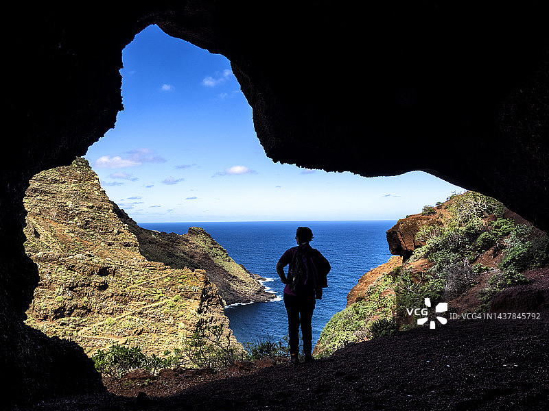 在拉帕尔马加那利岛，一个女人的剪影沿着海边的山路走在山洞里。图片素材