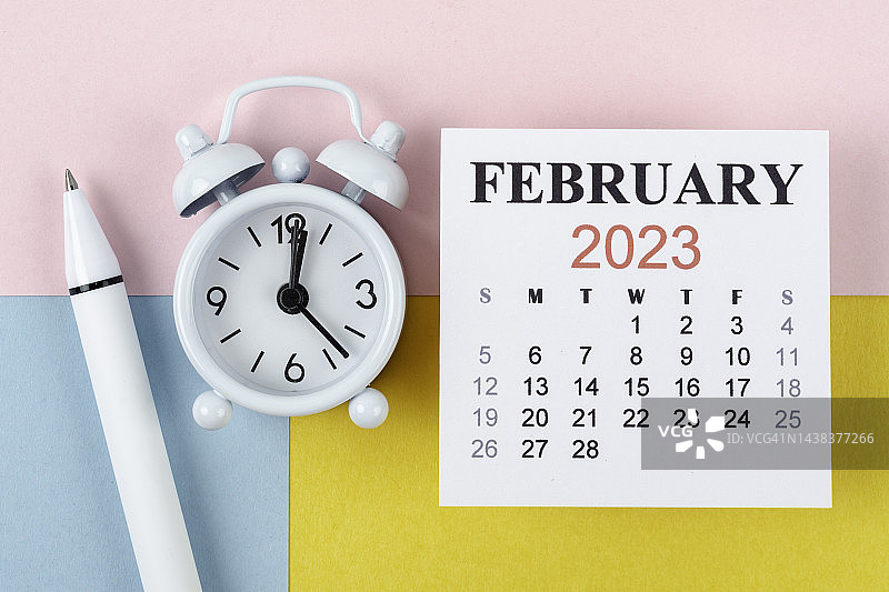 日历桌2023:2月是组织者用闹钟和双色纸背景白笔做计划和截止日期的月份。图片素材