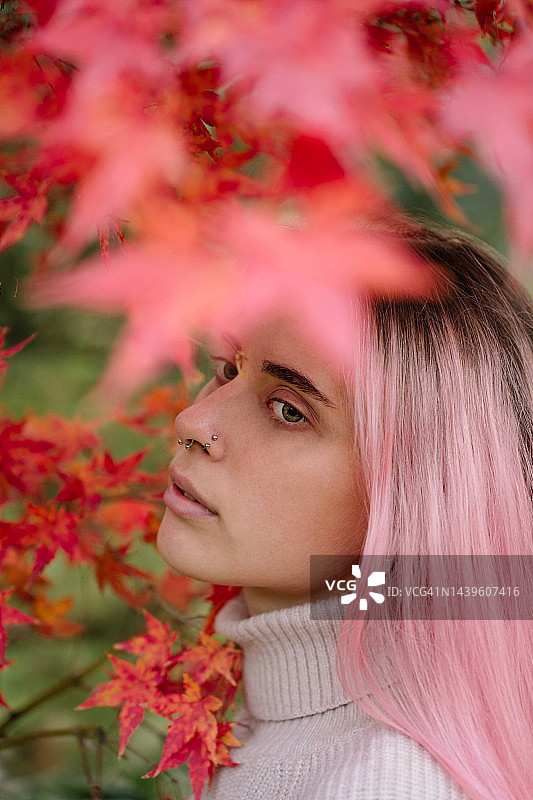 染着粉红色长发的年轻女子在公园里享受着秋天的心情，树叶背景是橙色和红色图片素材