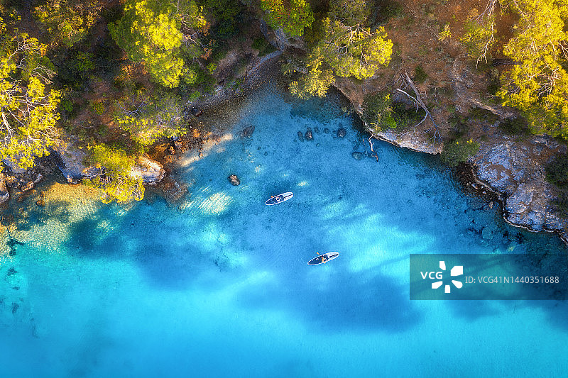 空中俯瞰人们在漂浮的sup板上，蓝色的大海，岩石，树木在夏天的日落。土耳其奥鲁德尼兹的蓝礁湖。热带景观。在清澈的水面上划皮艇。活跃的旅游。独木舟俯视图图片素材