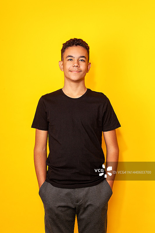 工作室肖像的13岁少年在黑色t恤对黄色背景图片素材