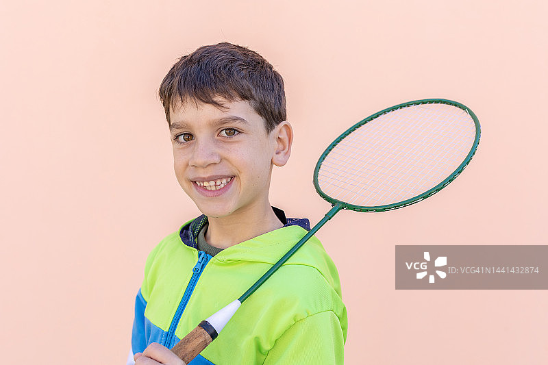 微笑的年轻白人男孩拿着羽毛球拍在户外孤立的墙图片素材