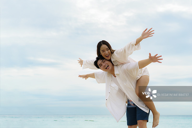 亚洲男子背着女友在泰国普吉岛的沙滩上度过暑假，他们看起来很开心很有趣。图片素材