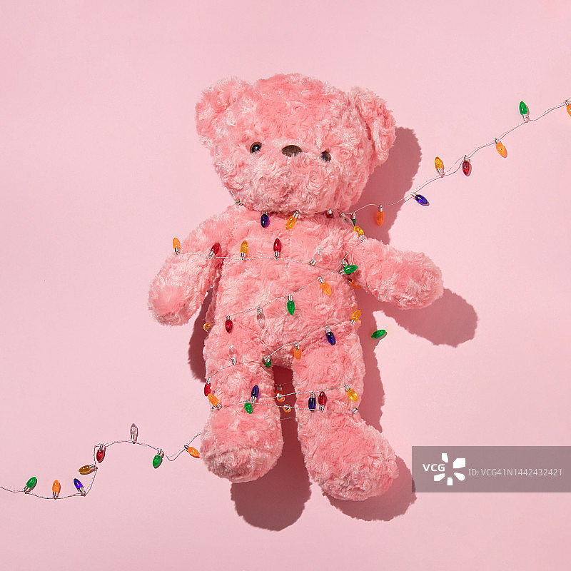 圣诞创意布局与粉色泰迪熊和圣诞灯在柔和的粉色背景。复古美学玩具概念。最小的庆祝想法。图片素材