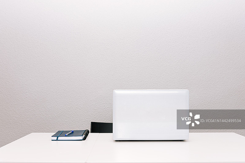 白色的桌椅。笔记本电脑和议程。远程工作的概念。灰色背景。图片素材