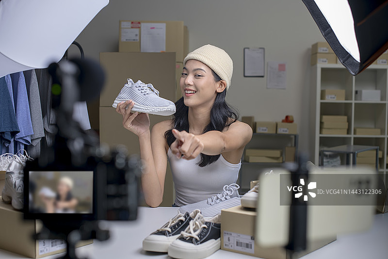 年轻的亚洲电子商务女企业主看着相机审查产品。图片素材