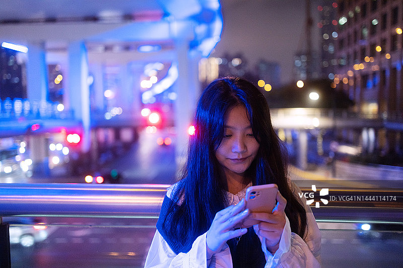 年轻的亚洲女子在城市人行桥上使用智能手机图片素材