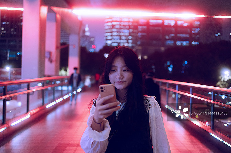 年轻的亚洲女子在城市人行桥上使用智能手机图片素材
