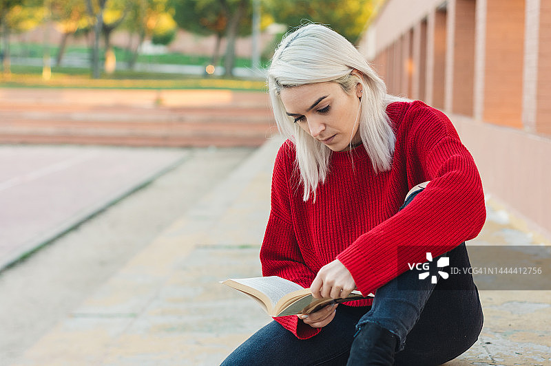 银发女孩坐着看书。穿着一件红毛衣。图片素材