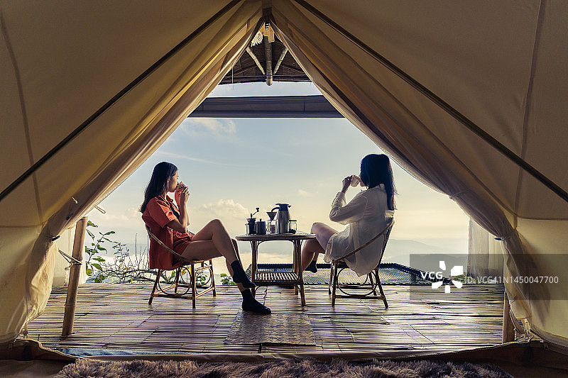 Two women sitting together making coffee with views of mountains, sea of ​​fog and sunlight. through tent view图片素材