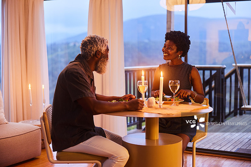 一对微笑的夫妇在他们有风景的家里边吃烛光晚餐边聊天图片素材