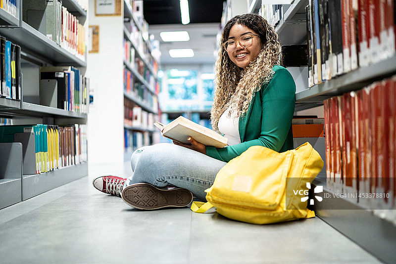 一个年轻的女学生坐在大学图书馆的地上图片素材