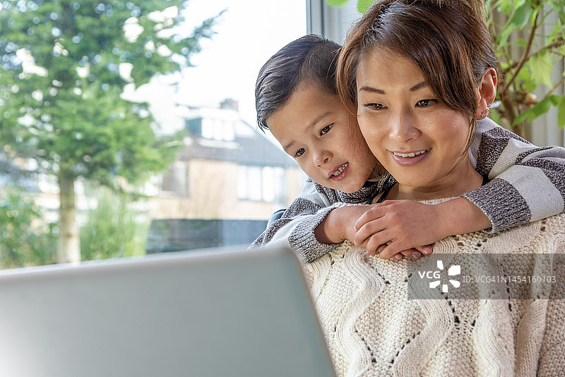 快乐的亚洲母亲和儿子在家里看着笔记本电脑图片素材