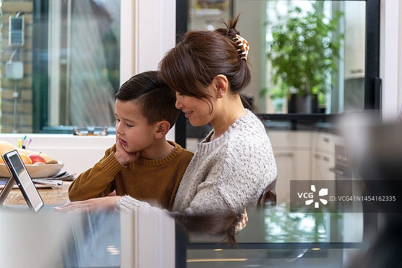 快乐的亚洲母亲和儿子在厨房看平板电脑图片素材