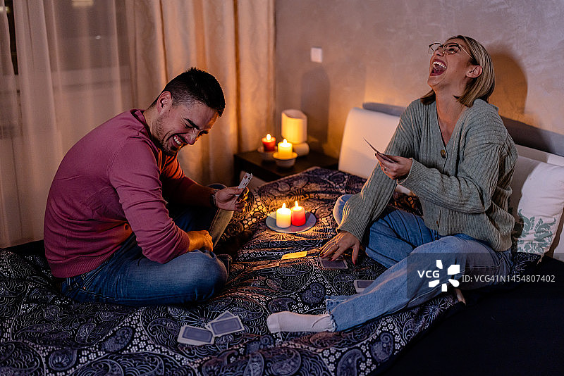 一对年轻夫妇在家里遭遇电力危机，正在玩纸牌游戏。图片素材