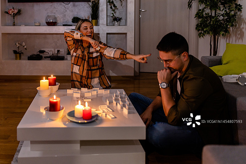 在一次精力充沛的危机中，一对年轻夫妇在黑暗中点着蜡烛玩多米诺骨牌。图片素材