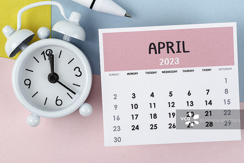 日历台2023:四月是组织者用闹钟和白笔在双色纸背景下计划和截止日期的月份。图片素材