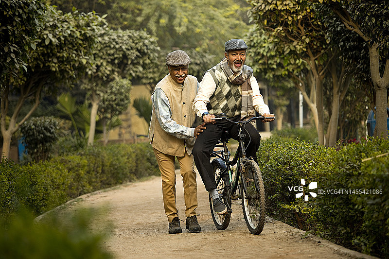 欣喜若狂的老人和朋友在公园学习骑自行车图片素材