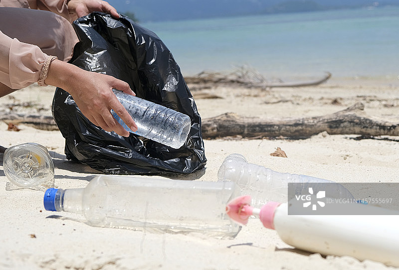 一个女人的手在收集塑料垃圾、水瓶和塑料瓶。海滩上有很多土她把它放进一个垃圾袋里。环境保护和减少全球变暖的概念图片素材