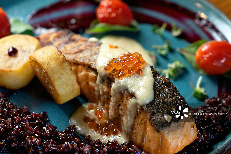 烤鲑鱼配蓝盘。配以蔬菜、三文鱼、酱汁和鱼子酱。软的焦点。特写镜头图片素材