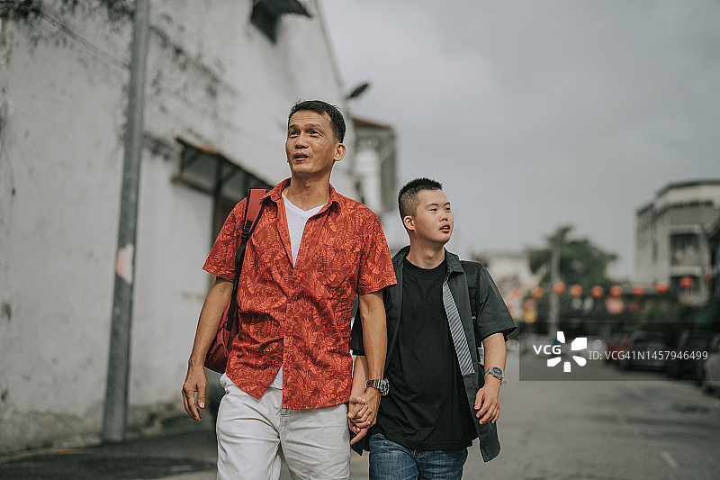 患有唐氏综合症的亚裔华人年轻人和父亲走在人行道上图片素材