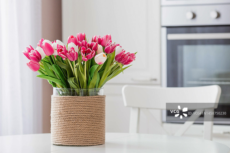 白色的桌子上放着一束郁金香。背景是斯堪的纳维亚风格的白色厨房内部。家庭舒适的概念。3月8日国际妇女节的概念。图片素材