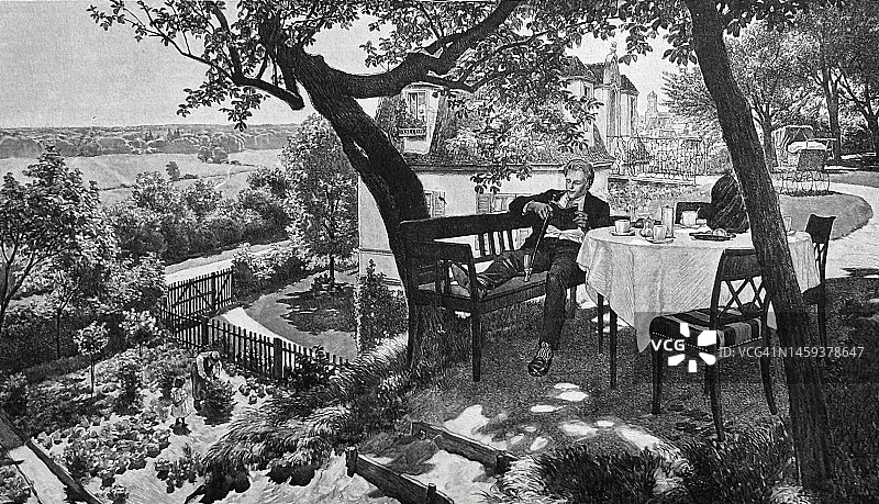 一个年轻人坐在高河边的花园餐厅的咖啡桌旁享受他的假期，一边看书图片素材