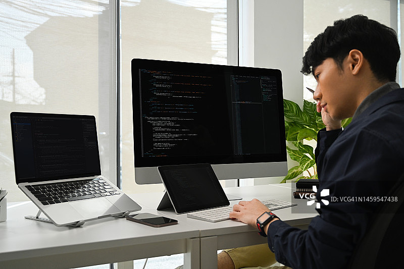 年轻程序员在电脑上工作，检查IT办公室的漏洞系统的编码。图片素材
