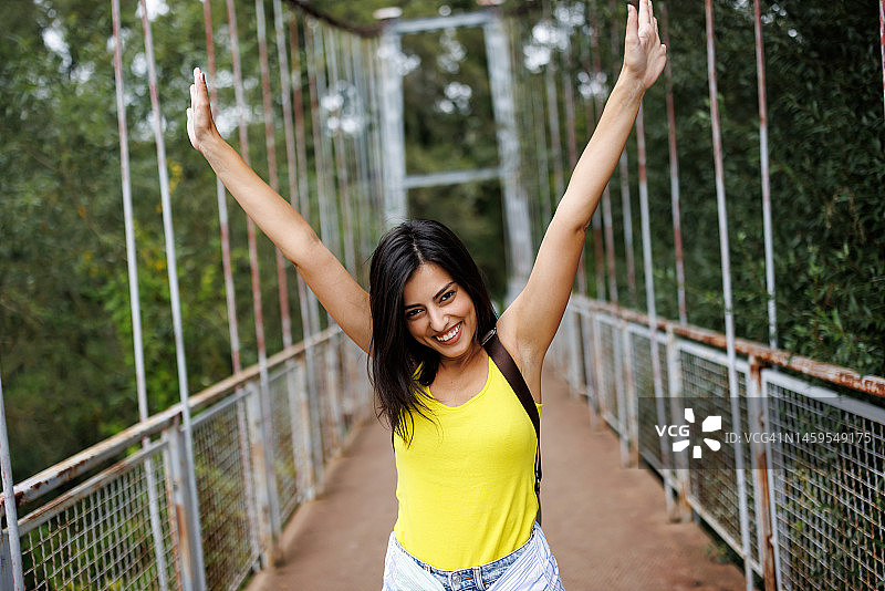 在阳光明媚的日子里，快乐的年轻女子走在大自然的人行桥上图片素材