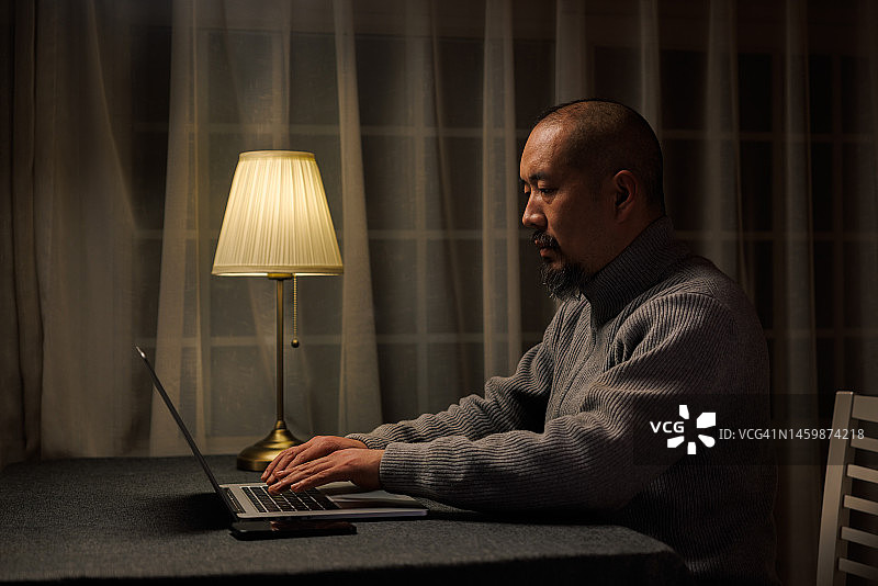 亚洲男人晚上用笔记本电脑工作图片素材