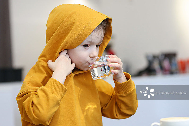 迷人的5岁女孩穿着黄色运动衫在当地的咖啡馆喝纯净水图片素材