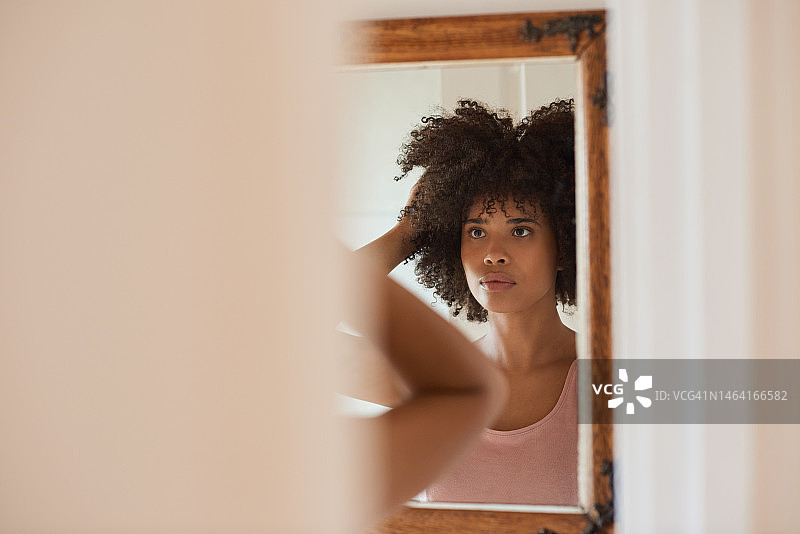 年轻的非洲妇女在浴室的镜子里看着自己的头发图片素材