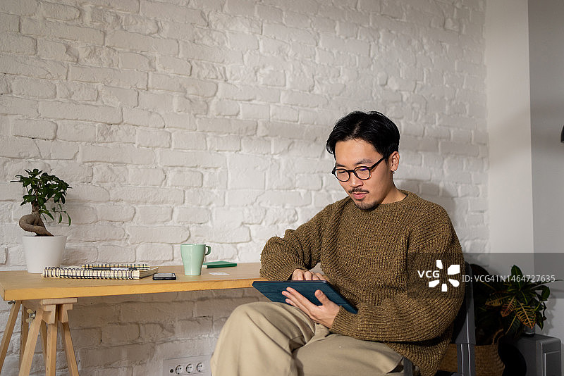 中国帅哥戴眼镜在他的家庭办公室在他的平板电脑上工作图片素材