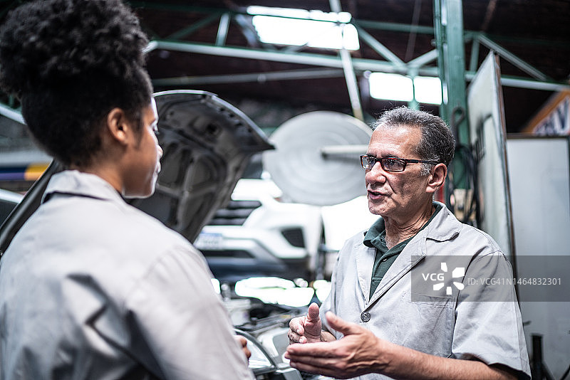 一个汽车修理工在修理厂和他的助手谈话图片素材