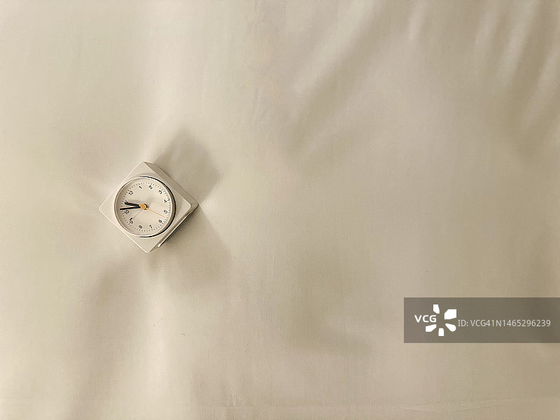 白色的小闹钟依偎在舒适的床上图片素材