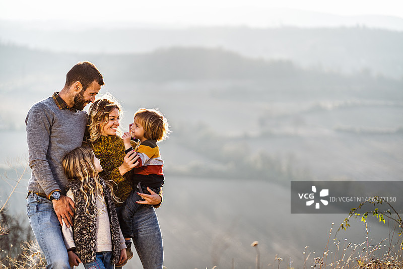 秋日小山上，年轻幸福的一家人在聊天。图片素材