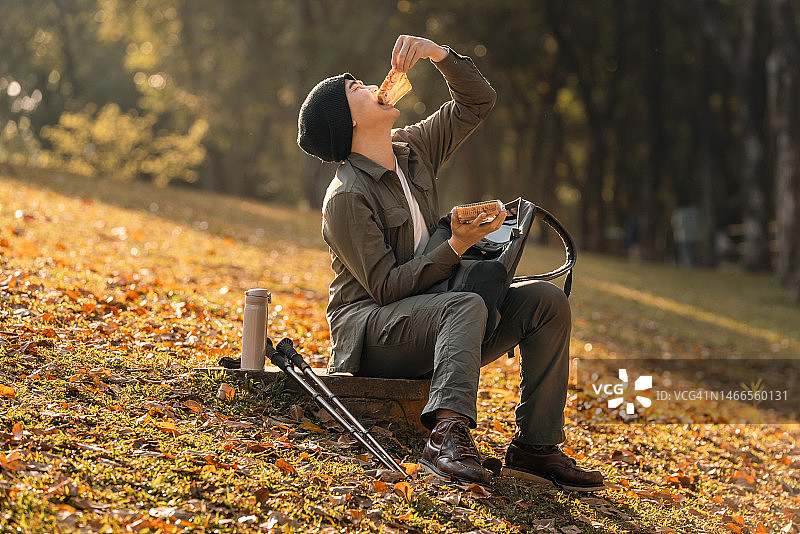 一名亚洲年轻男子正在大自然中吃面包休息。图片素材