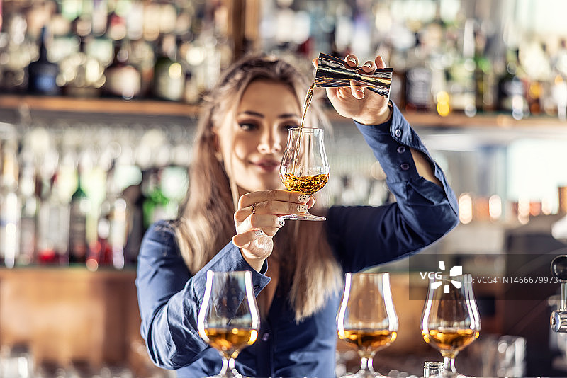 年轻的女调酒师专业地把朗姆酒或白兰地从钢瓶倒进玻璃杯里。图片素材
