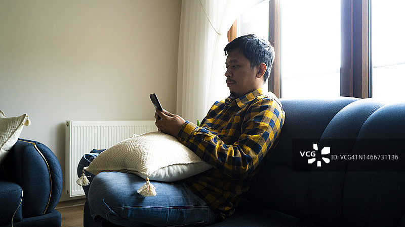 亚洲年轻人在客厅使用智能手机图片素材