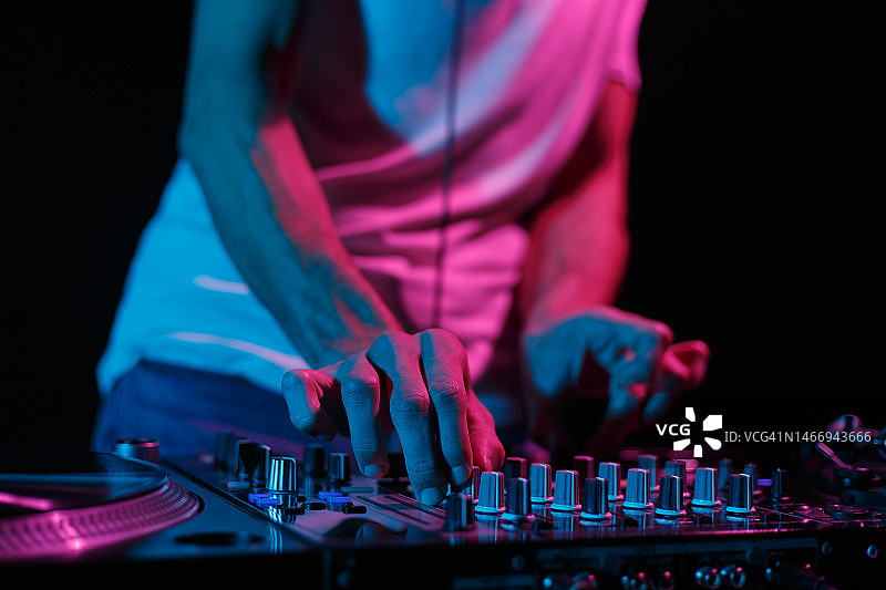 俱乐部DJ在派对上用混音器混合音乐。在夜总会演奏的音乐节目主持人的手图片素材