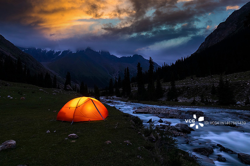 帐篷在戏剧性的日落在山的背景。图片素材