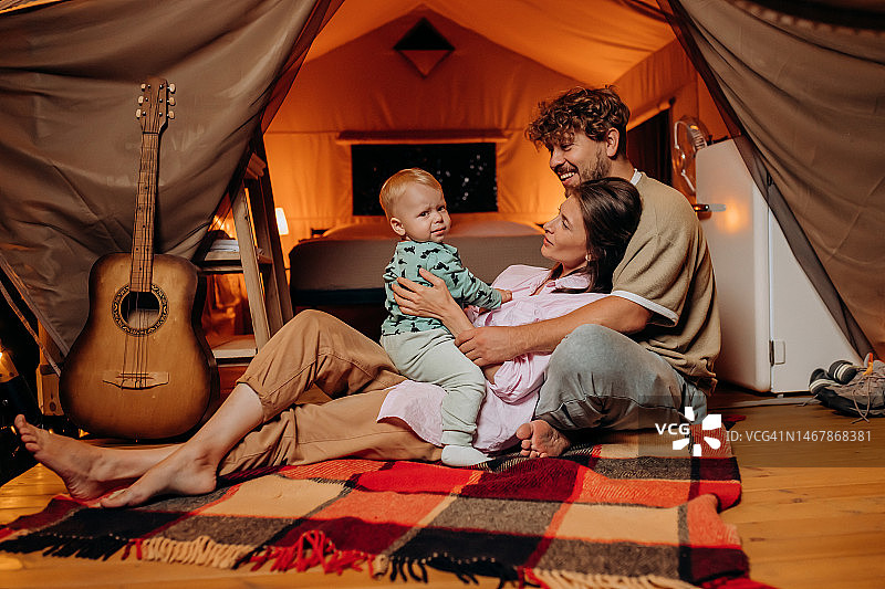 快乐的家庭和可爱的宝宝一起玩耍，在夏天的晚上一起露营。户外休闲休闲的豪华露营帐篷。生活方式的概念图片素材