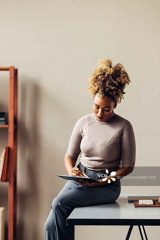 一个金发卷毛的漂亮女商人拿着笔在平板电脑上工作图片素材